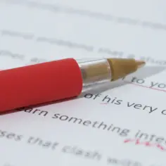 Czerwony długopis nad tekstem z zaznaczonymi błędami na białym papierze.