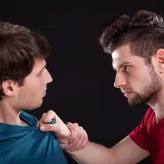 Dwóch mężczyzn w profilu, jeden chwyta drugiego za koszulkę.